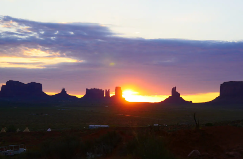 Sunset over Monument Valley, casting warm light on iconic rock formations against a colorful sky.